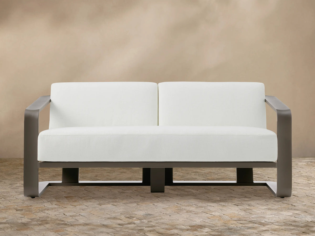 Sonoma outdoor aluminum sofa, Savona Snow white cushions, dark bronze frame. Front view on stone patio.