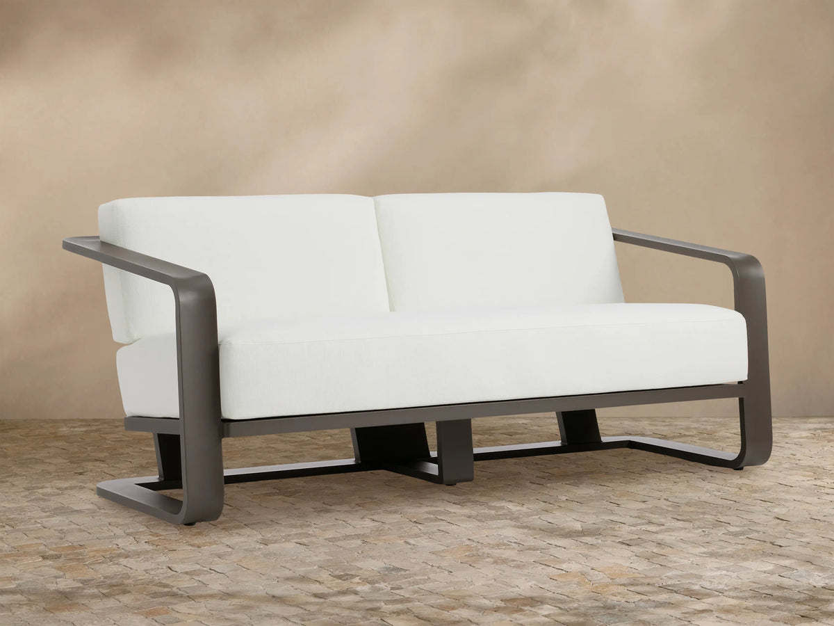 Sonoma outdoor aluminum sofa, Savona Snow white cushions, dark bronze frame. Front view on stone patio.