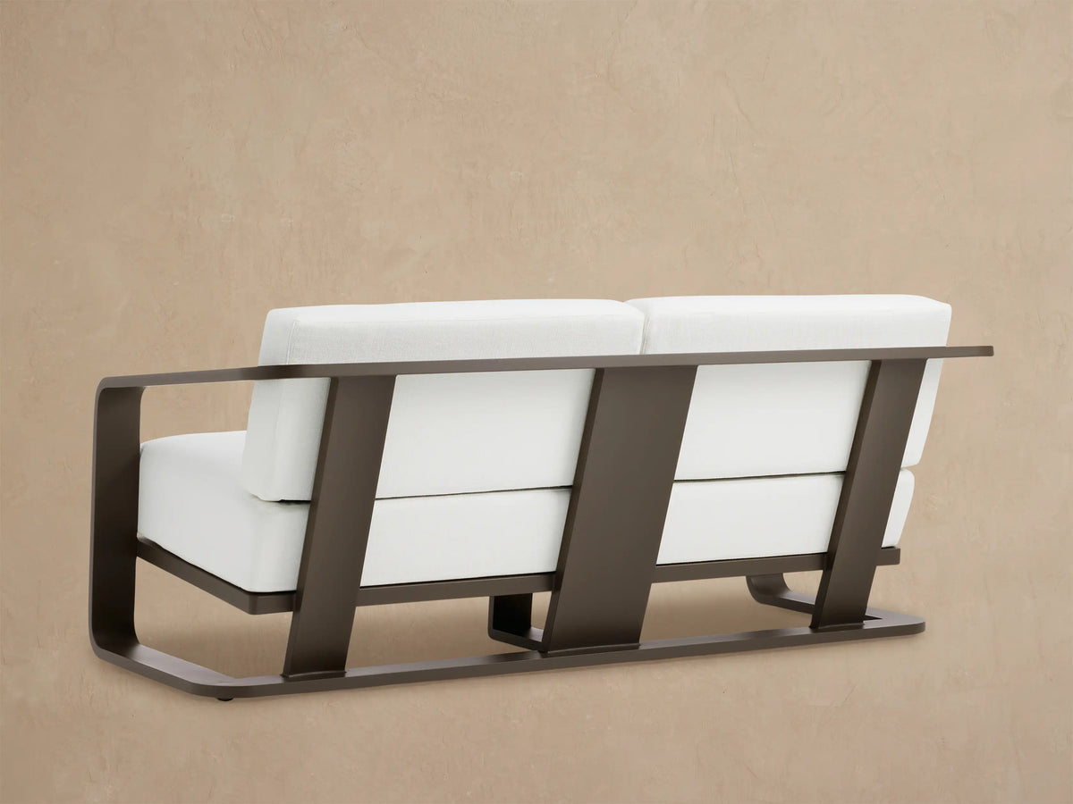 Close-up of Sonoma Outdoor Aluminum Sofa's dark bronze armrest and bright white Savona Snow cushions.