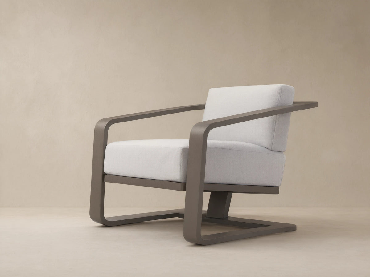 Modern dark gray aluminum Sonoma Outdoor Lounge Chair with thick white Savona Snow cushions, angled right on a tiled patio.