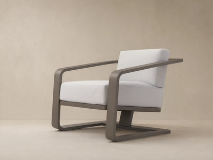 Modern dark gray aluminum Sonoma Outdoor Lounge Chair with thick white Savona Snow cushions, angled right on a tiled patio.