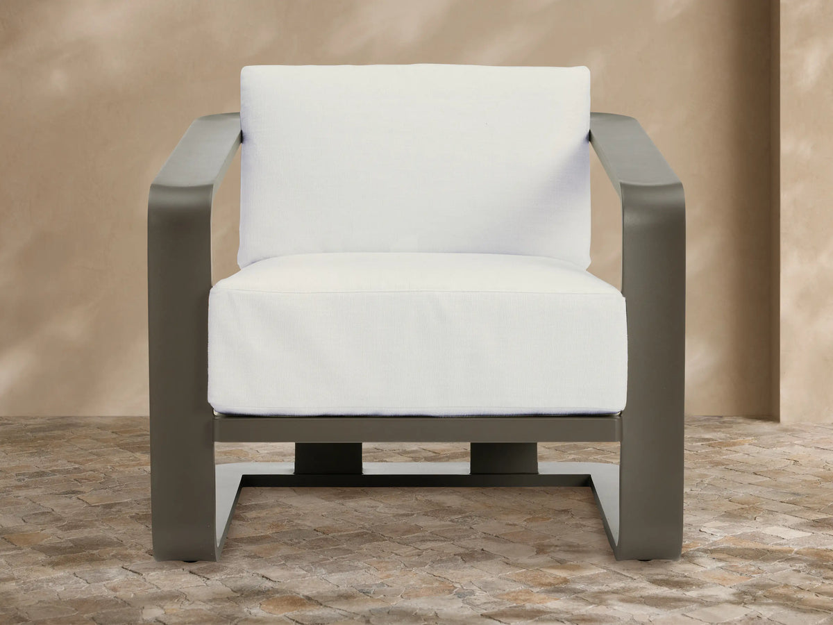 Modern dark gray aluminum Sonoma Outdoor Lounge Chair with thick white Savona Snow cushions, angled right on a tiled patio.
