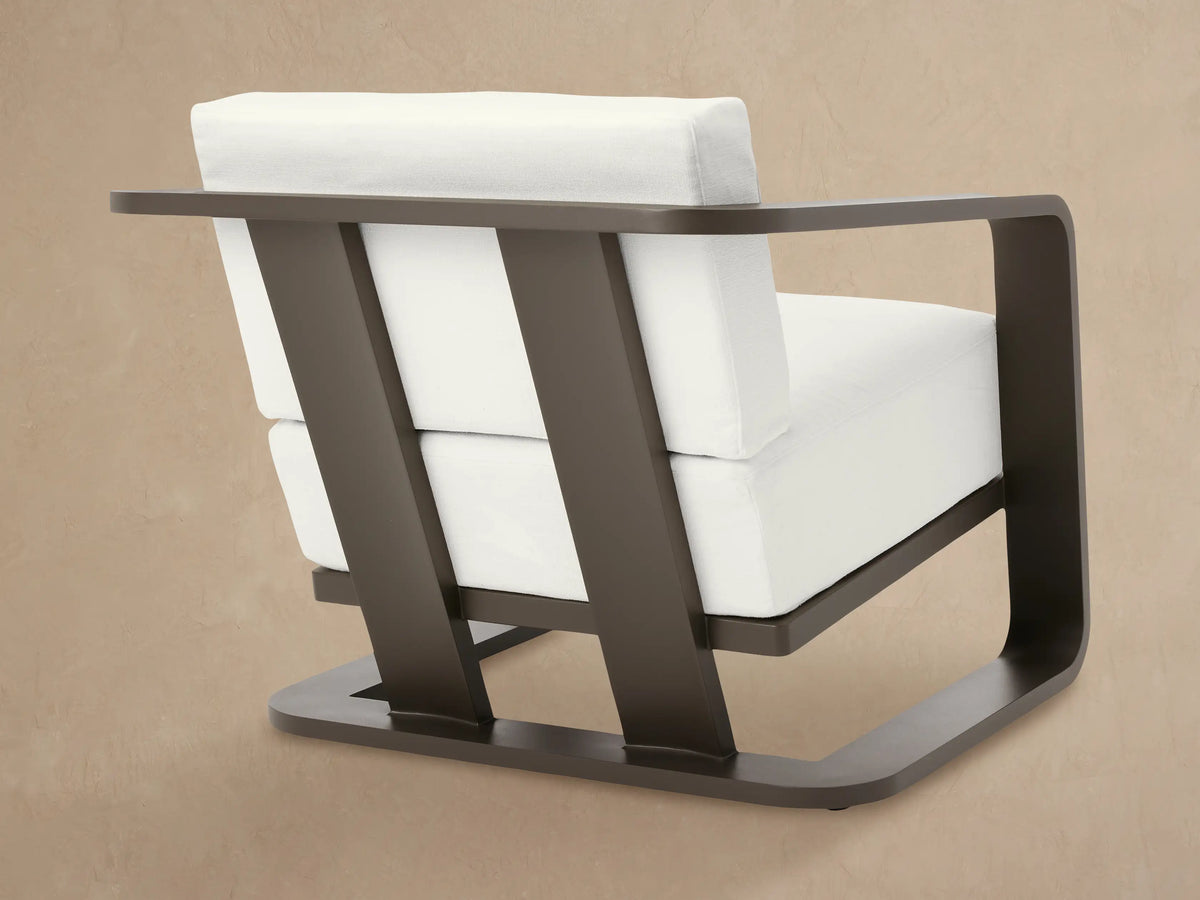 Angled close-up of Sonoma Outdoor Aluminum Lounge Chair's curved dark brown armrest and white Savona Snow cushions.