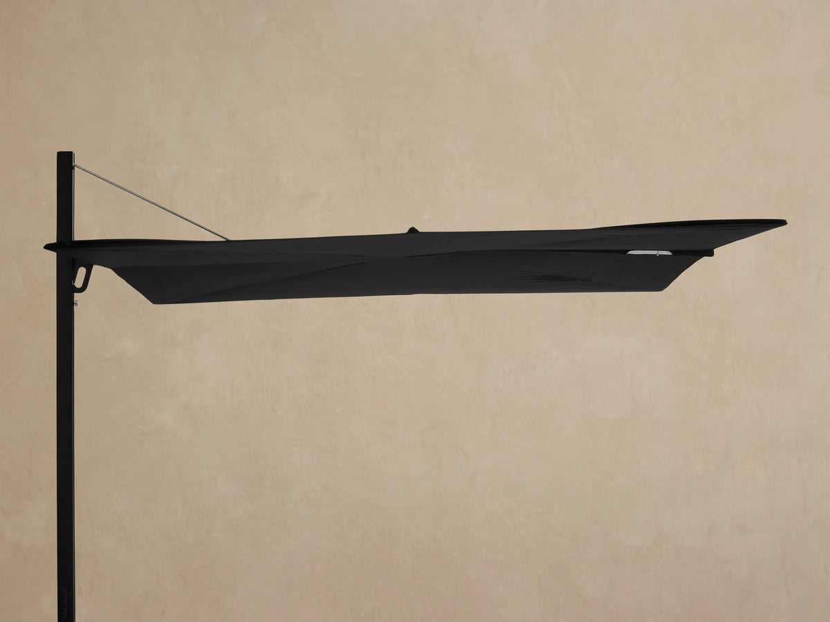 Black, closed Spectra Outdoor Umbrella angled horizontally, with a black frame & square mobile base on a light patio.
