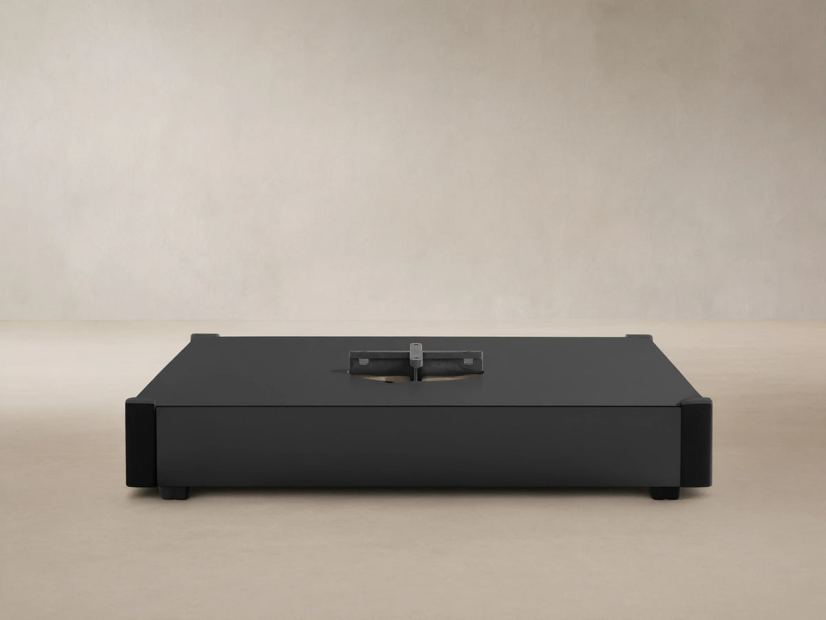 Black rectangular Spectra Outdoor Umbrella Base with a central silver cross-shaped mounting plate against a light wall.
