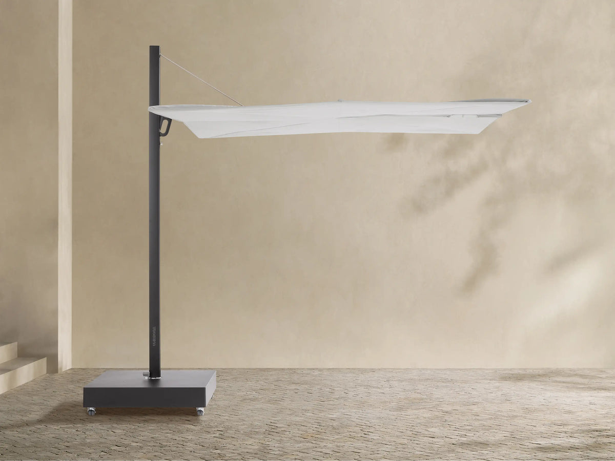 Closed Spectra Outdoor Square Umbrella, light off-white canopy, dark gray frame & wheeled base, against a beige wall.
