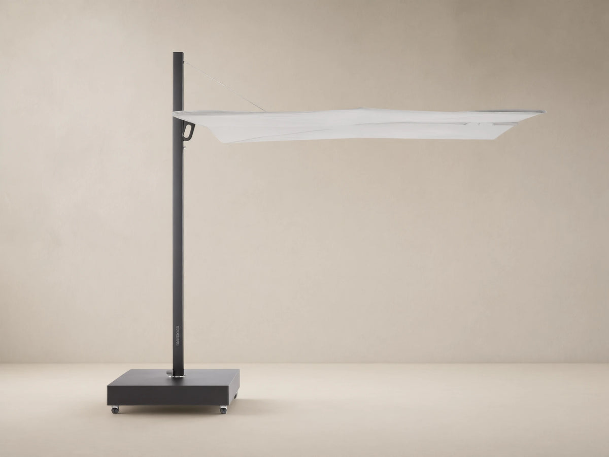 Closed Spectra Outdoor Square Umbrella, light off-white canopy, dark gray frame & wheeled base, against a beige wall.