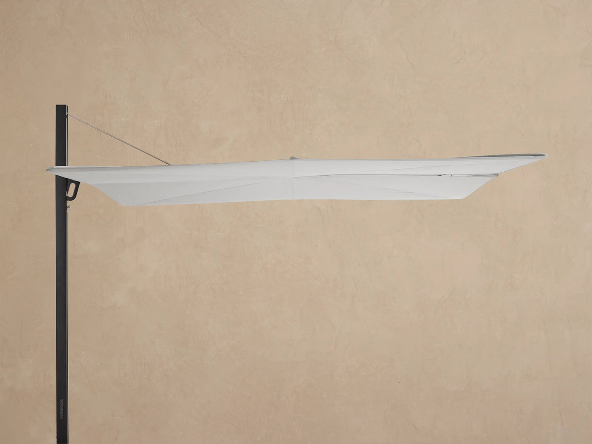 Spectra Outdoor Umbrella with white closed canopy, black pole, and square wheeled base on pavers against a beige wall.