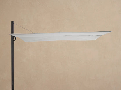 Spectra Outdoor Umbrella with white closed canopy, black pole, and square wheeled base on pavers against a beige wall.