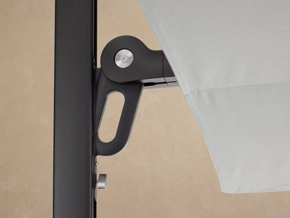 Side view of Spectra Outdoor Umbrella with closed, horizontal off-white canopy showing geometric folds, on a dark frame against a beige wall.