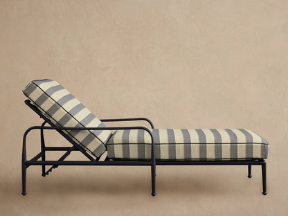 Four gray and white striped Surrey Outdoor Chaise lounges with dark frames and navy pillows beside a pool.