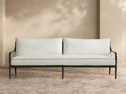 Surrey Outdoor Sofa: black metal frame, two white cushions with black piping, front view, against a beige wall.