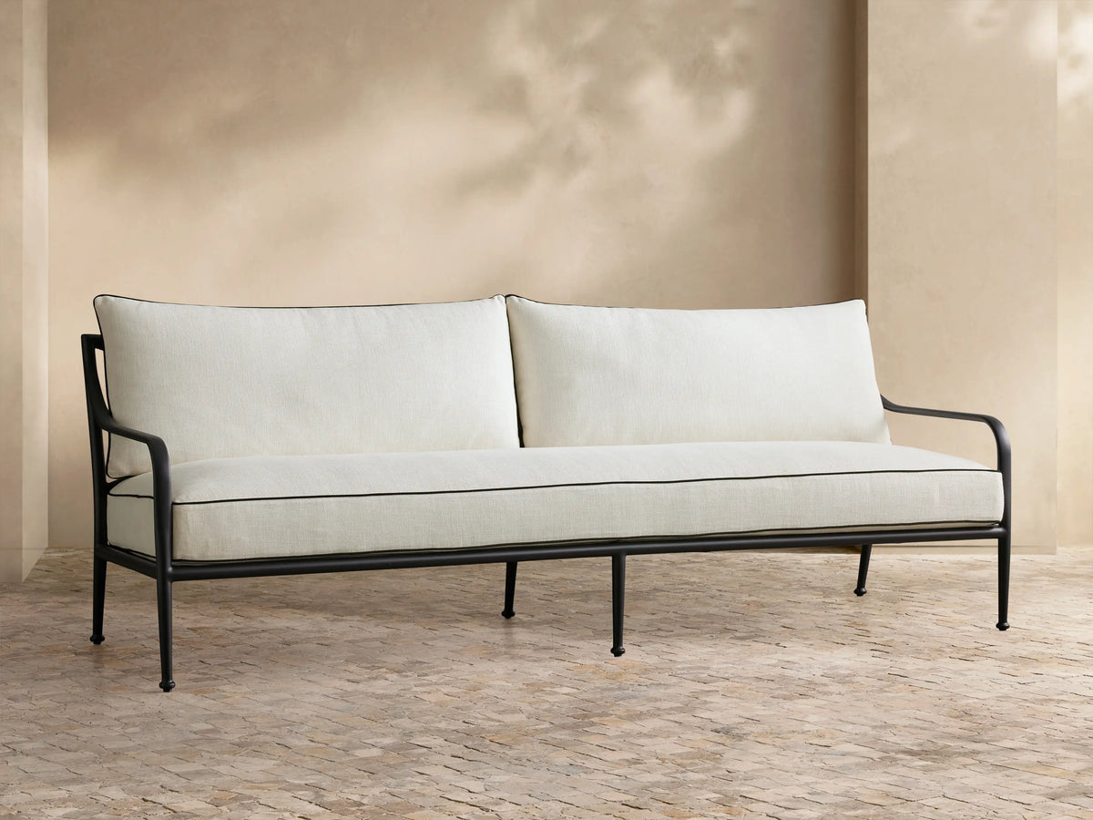 Full view of the beige cushioned Surrey Outdoor Sofa with a black metal frame, navy and striped pillows.