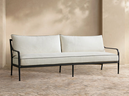 Full view of the beige cushioned Surrey Outdoor Sofa with a black metal frame, navy and striped pillows.