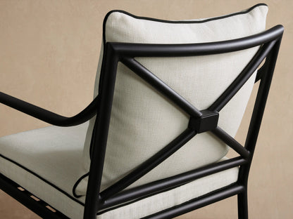Surrey Outdoor Dining Arm Chair, front, black aluminum frame, light cream cushions with black piping, on a textured stone floor.