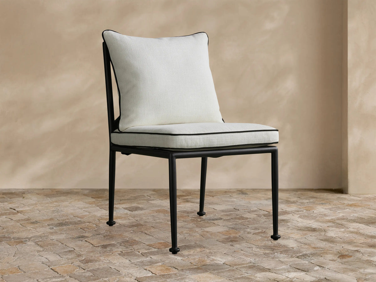 Surrey Outdoor Dining Side Chair with a sleek black metal frame, plump white cushions with black piping, on a tiled patio.