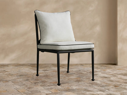 Surrey Outdoor Dining Side Chair with a sleek black metal frame, plump white cushions with black piping, on a tiled patio.