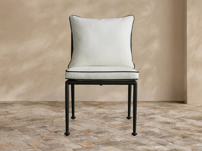 Black Surrey Outdoor Dining Side Chair with cream cushions and an X-back design, shown around a dining table on a patio.