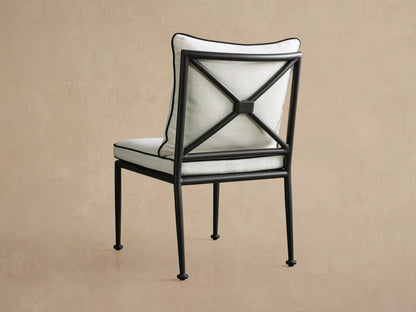 Surrey Outdoor Dining Side Chair with dark X-back frame & off-white cushions featuring black piping, viewed from back-right.