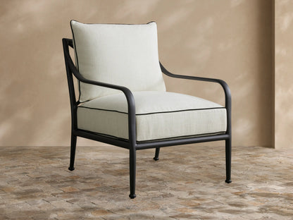 Surrey Outdoor Lounge Chair, black aluminum frame, light cream cushions with black piping, on a stone patio.