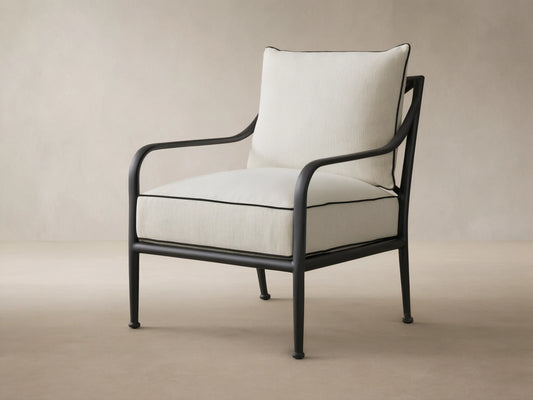 Surrey Outdoor Lounge Chair, black aluminum frame, light cream cushions with black piping, on a stone patio.