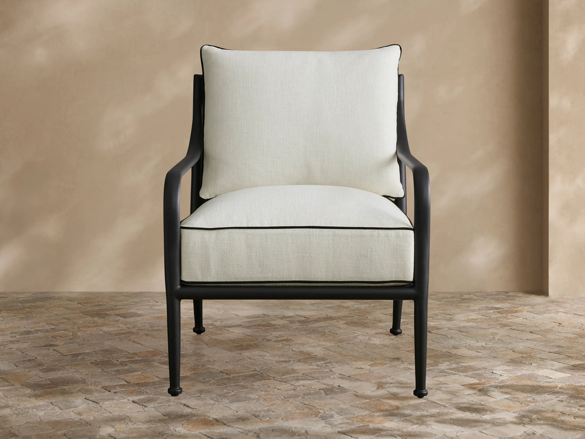 Outdoor view of two Surrey Outdoor Lounge Chairs, sofa, and coffee table. Black frames, cream cushions with black piping, on a stone patio.