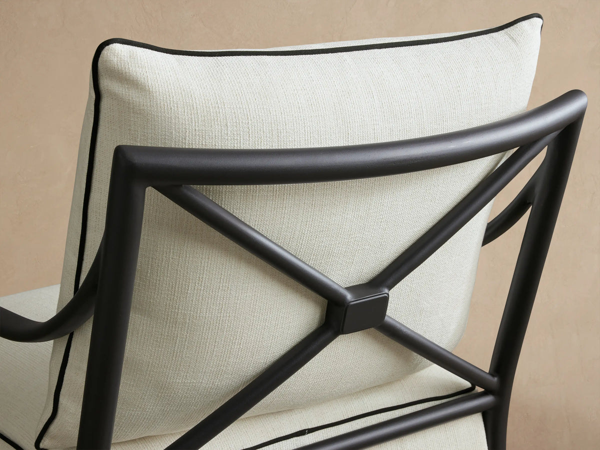Surrey Outdoor Lounge Chair with dark aluminum frame, off-white cushions and black piping, on a tiled patio.