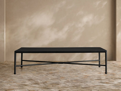 Black Surrey Outdoor Coffee Table, rectangular with slatted top and X-shaped base, on a tiled patio floor against a beige wall.