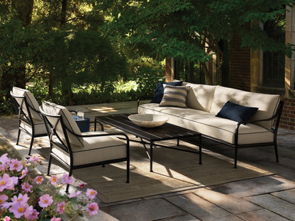 Black Surrey Outdoor Coffee Table, rectangular with slatted top and X-shaped base, on a tiled patio floor against a beige wall.