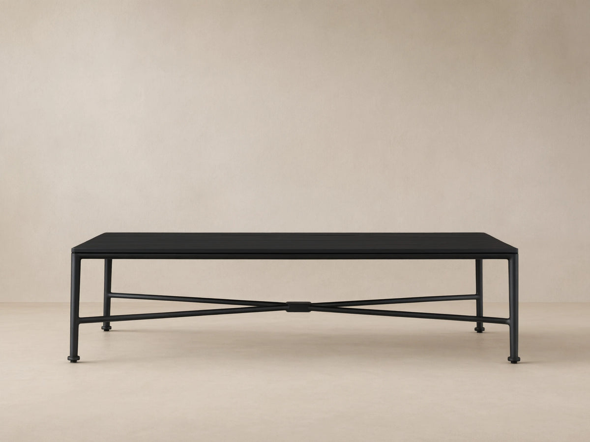 Black Surrey Outdoor Coffee Table, rectangular with slatted top and X-shaped base, on a tiled patio floor against a beige wall.