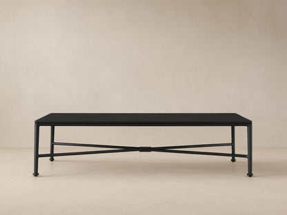 Black Surrey Outdoor Coffee Table, rectangular with slatted top and X-shaped base, on a tiled patio floor against a beige wall.
