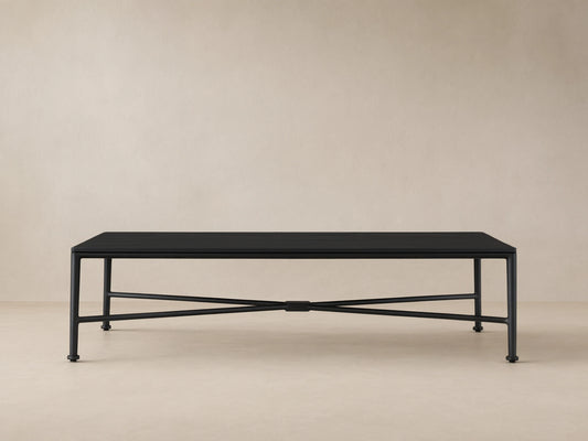 Black Surrey Outdoor Coffee Table, rectangular with slatted top and X-shaped base, on a tiled patio floor against a beige wall.