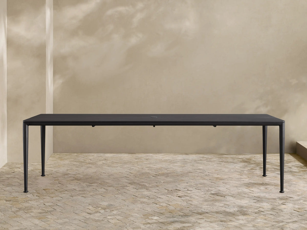 Dark gray powder-coated aluminum Surrey Outdoor Dining Table, long and rectangular, with an umbrella hole, in an outdoor patio.