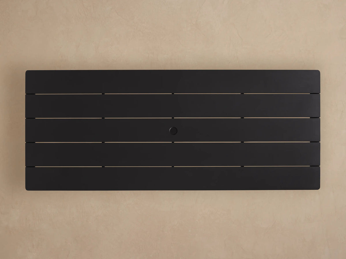 Close-up of Surrey Outdoor Dining Table, dark grey powder-coated aluminum with textured, slatted top & silver lines. Table leg visible.