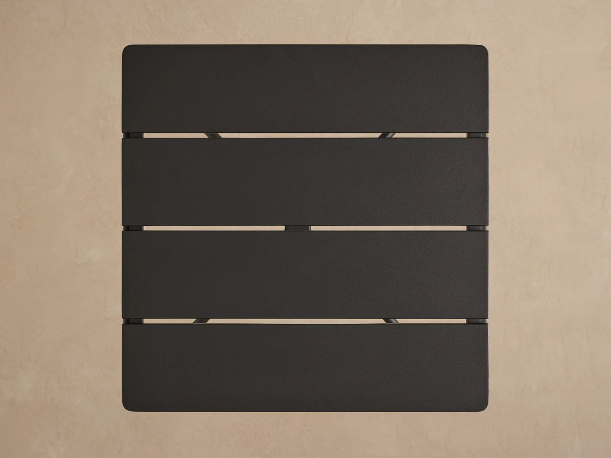 Surrey Outdoor End Table. Square charcoal gray slatted top with matte black aluminum frame, viewed from a slight angle.
