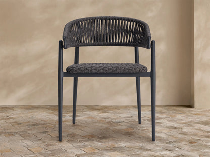 Talia Outdoor Dining Chair. Dark gray woven rope back and seat, sleek dark frame, on a textured stone floor.