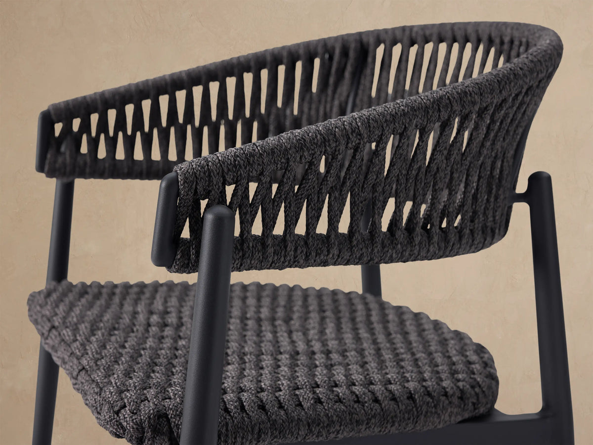 Dark gray Talia Outdoor Dining Chair with woven rope back and seat, sleek metal frame, seen from the front on a tiled patio.