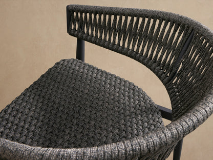 Front view of Talia Outdoor Aluminum Lounge Chair, dark gray woven rope back and seat, charcoal aluminum frame, on textured floor.