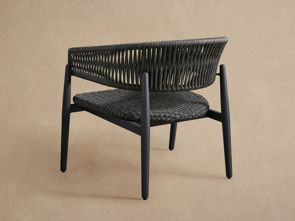 Close-up of Talia Outdoor Lounge Chair, dark gray woven rope seat and backrest, black aluminum frame, beige background.