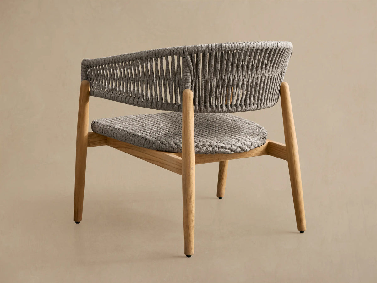 Close-up, angled view of Talia Outdoor Teak Lounge Chair. Grey woven rope seat & backrest on light natural teak wood frame.