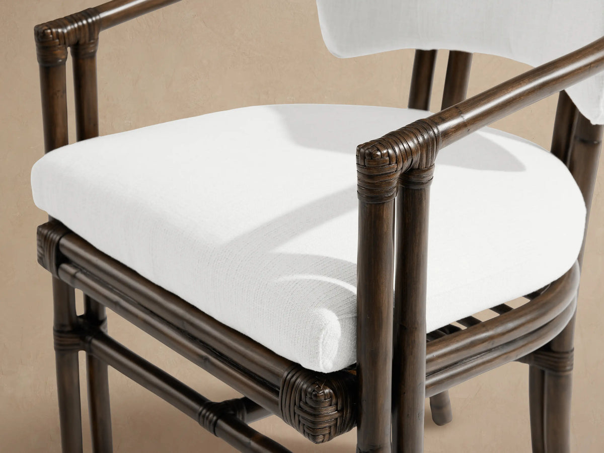 Van Sunroom Dining Chair, dark rattan frame with white back & seat cushions, front view on a patio floor against a beige wall.