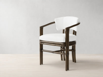 Dark brown rattan pole Van Sunroom Dining Chair with white cushions, slightly angled, on a light stone tile floor.
