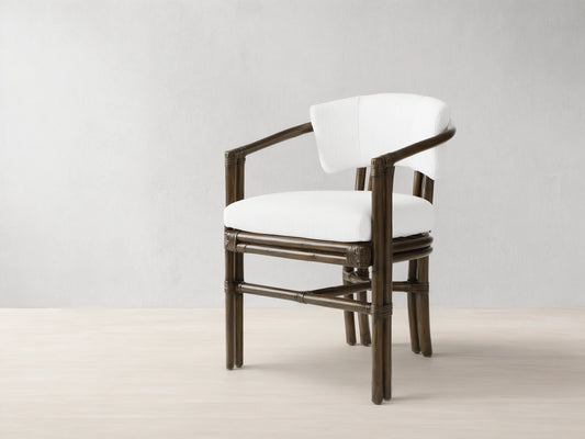 Dark brown rattan pole Van Sunroom Dining Chair with white cushions, slightly angled, on a light stone tile floor.