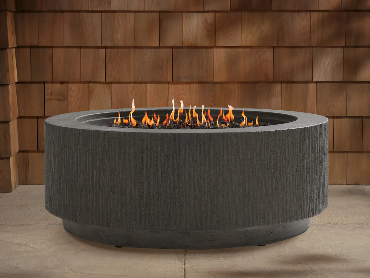 Wilmar Round Propane Fire Pit, dark gray textured concrete with active flames in a black lava rock bed, on a patio.