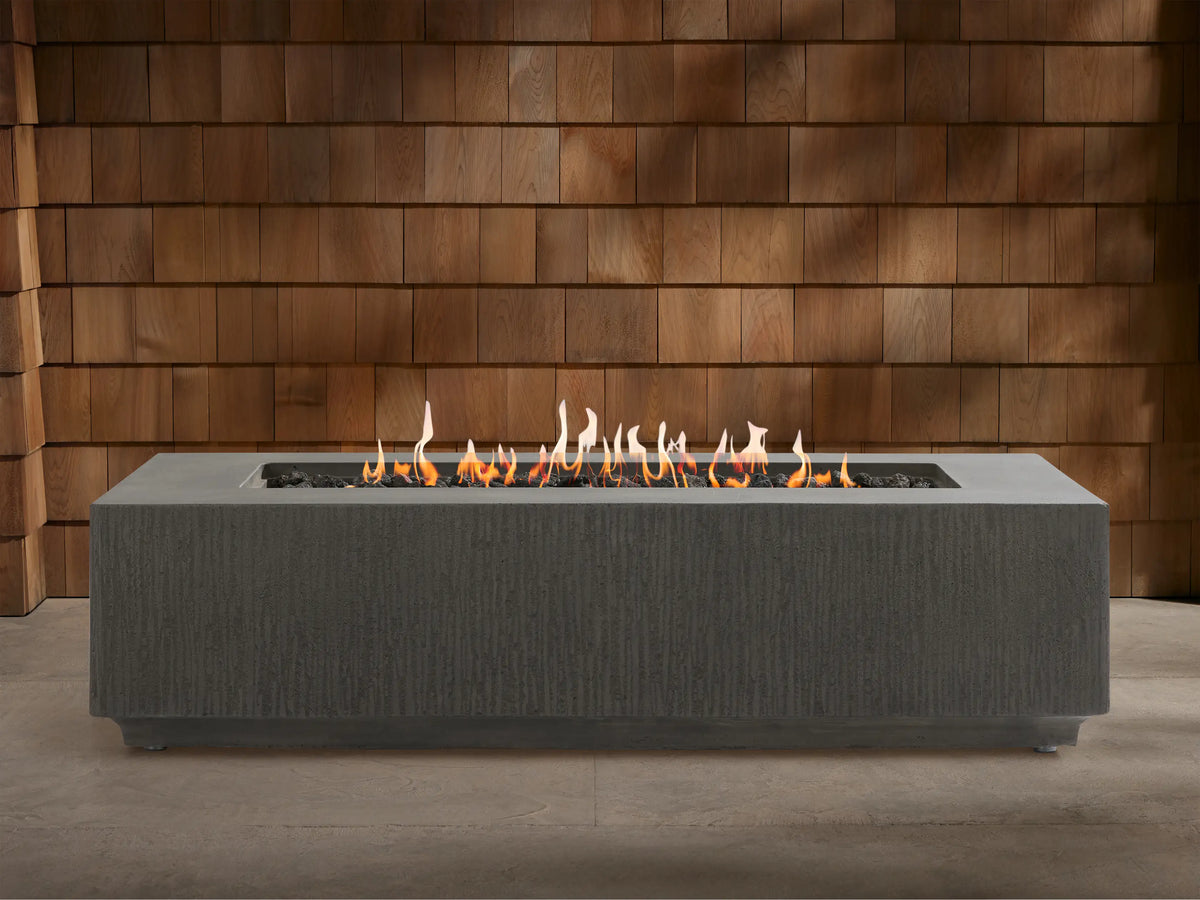 Wilmar Rectangular Propane Fire Pit, dark gray textured concrete, with bright flames rising from black lava rocks.