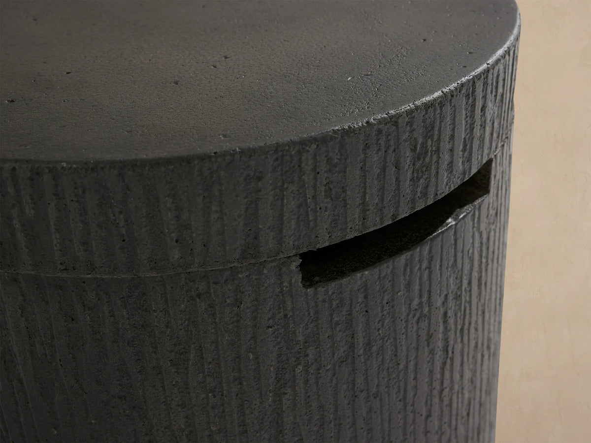 Cylindrical dark gray concrete Wilmar Fire Pit Tank Cover with bark-like texture, flat top, and horizontal slot.