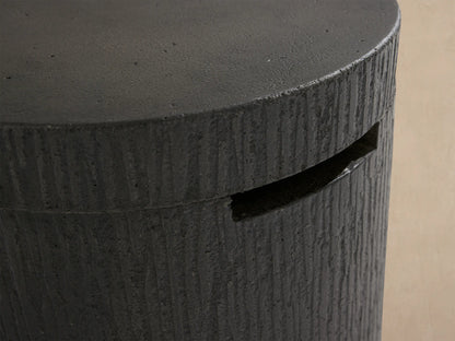 Cylindrical dark gray concrete Wilmar Fire Pit Tank Cover with bark-like texture, flat top, and horizontal slot.