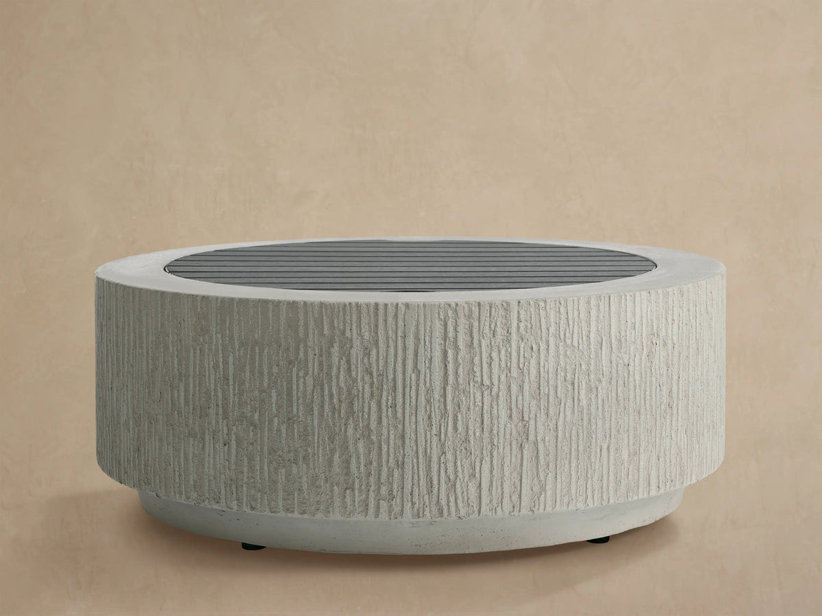 Wilmar Round Propane Fire Pit in Fog Chiseled, light grey concrete with vertical grooves, filled with black lava rock.
