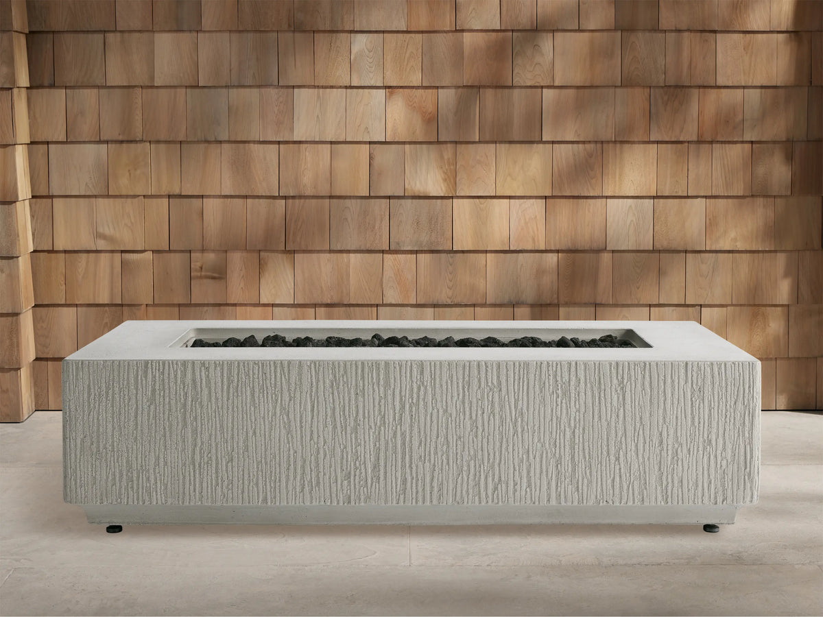 Wilmar Rectangular Natural Gas Fire Pit, gray concrete with textured sides, bright flames over black lava rock. Wooden shingle wall.