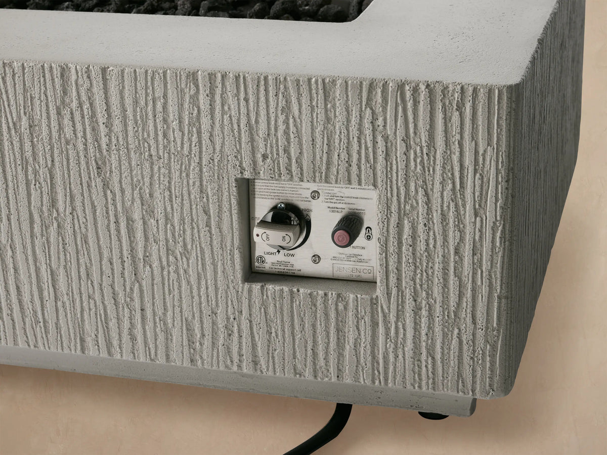 Rectangular Wilmar fire pit, textured light gray concrete with a black slatted top cover, shown frontally against a beige wall.